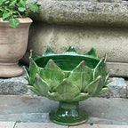A green glazed ceramic planter shaped like an artichoke, set outdoors on stone steps next to a potted plant.